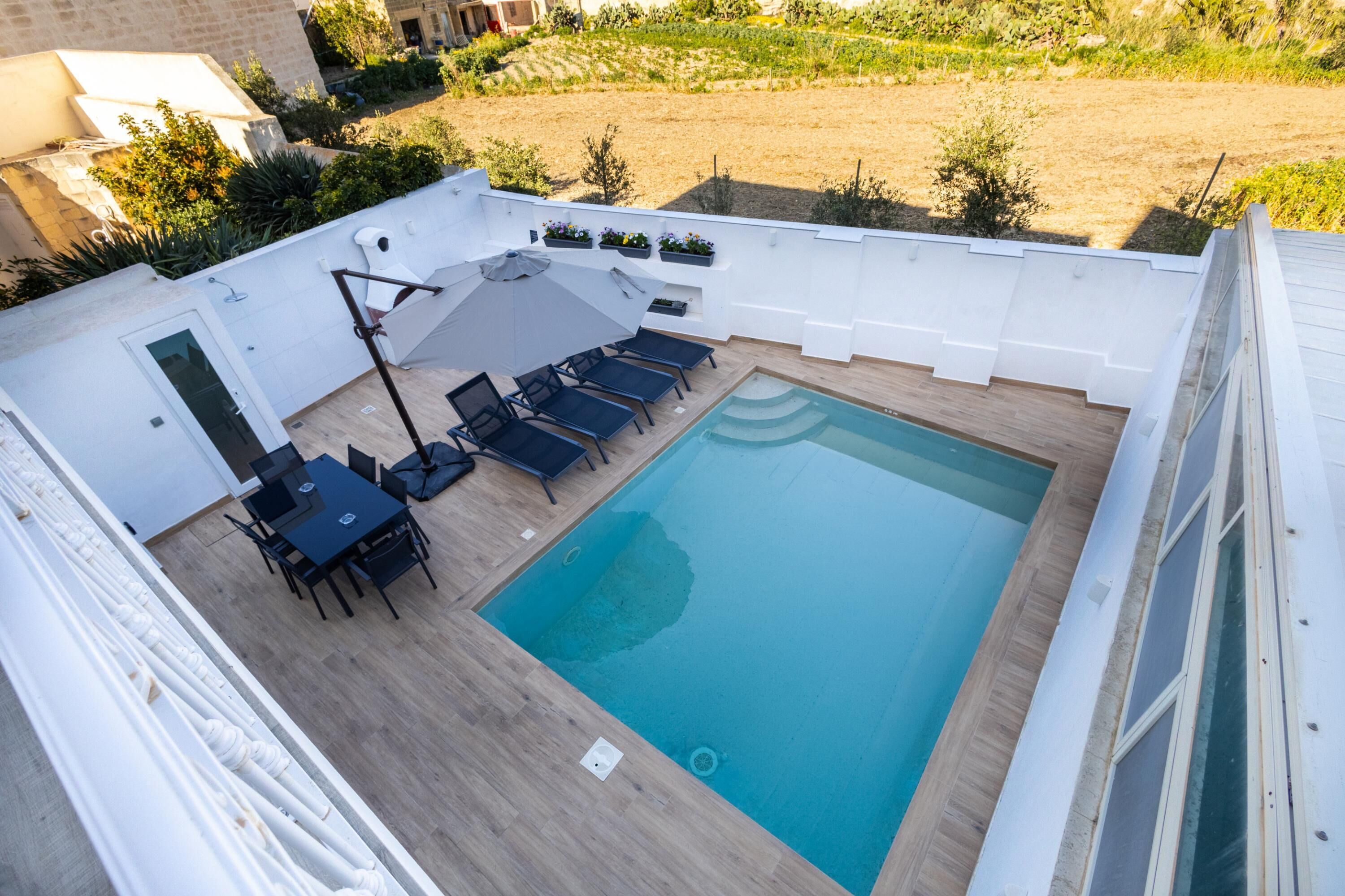 A rooftop swimming pool with a sun lounger, a table with chairs, and a small garden area.