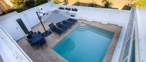 A rooftop swimming pool with a sun lounger, a table with chairs, and a small garden area.