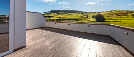 A balcony with a view of a green landscape and a hill.