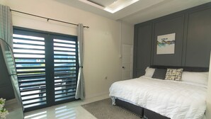 Une chambre avec un lit, une porte donnant sur une vue agréable, une œuvre d’art accrochée au mur et une fenêtre du sol au plafond.