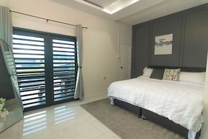 Une chambre avec un lit, une porte donnant sur une vue agréable, une œuvre d’art accrochée au mur et une fenêtre du sol au plafond.