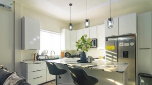 Une cuisine moderne avec des meubles blancs, des appareils en acier inoxydable et deux tabourets de bar.