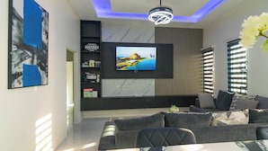 Un salon moderne avec un téléviseur à écran plat fixé au mur, un canapé, une table à manger et un luminaire suspendu au plafond.