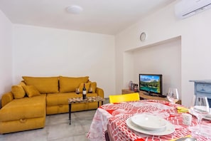 A living room with a sofa, a dining table set with plates and glasses, a television, and a clock on the wall. - Rural Apt Arya: Garden & BBQ, Šmarje, Slovenia (Šmarje)