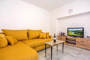 A living room with a yellow sofa, a small table with wine glasses, a television on a wooden stand, and a clock on the wall. - Rural Apt Arya: Garden & BBQ, Šmarje, Slovenia (Šmarje)
