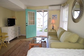 A room with a teal door, a white sofa, a small table, a television, and a lamp. - My Three Suns - Creek Front in Garden City Beach (Garden City)