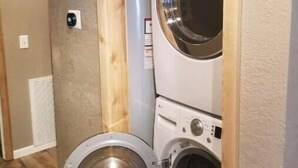 Een kleine wasruimte met een voorlader wasmachine en droger, houten ombouw en een zichtbare ventilatieopening in de muur.