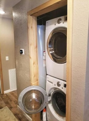 A compact laundry room with a front-loading washer and dryer, wooden framing, and a visible vent on the wall. - Charming 4-bedroom cabin with AC in peaceful Rhododendron (Rhododendron)