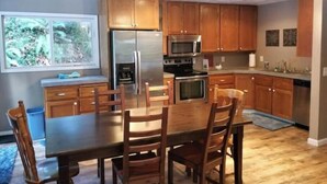 Een keuken met houten kasten, roestvrijstalen apparatuur en een eettafel met stoelen.