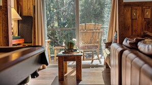 Un intérieur en bois avec un canapé, une table agrémentée d’un objet décoratif et une vue sur l’extérieur, visible à travers une porte vitrée.