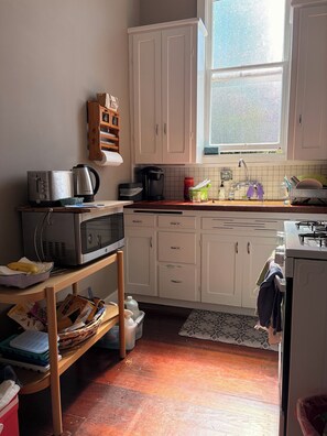 Eine Küche mit weißen Schränken, einer Mikrowelle, einem Toaster, einer Kaffeemaschine und einem Fenster mit Blick auf Grünflächen.
