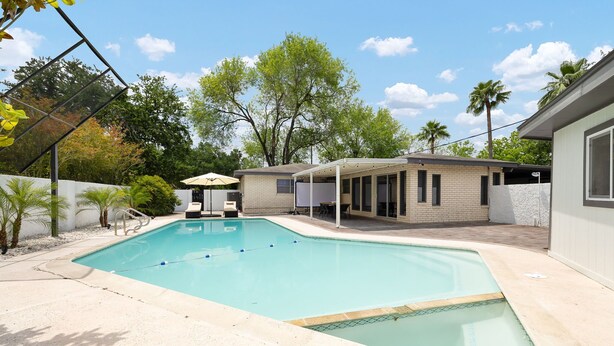 A swimming pool with a sunshade, a covered patio area, and a brick building in the background. - Pool and Pool House in McAllen (McAllen)