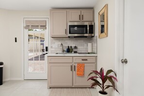 Una cocina con armarios color beige, un microondas de acero inoxidable, un fregadero y una planta en maceta.