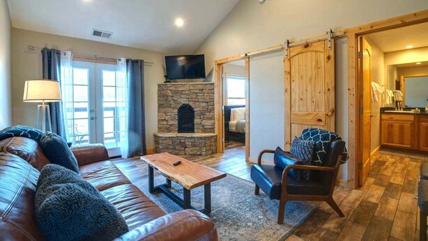 Ein Wohnzimmer mit Kamin aus Stein, einer Ledersofa, einem Holztisch und Blick zur Küche.