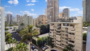A high-rise residential building with multiple balconies, a parking area, and surrounding greenery. - Waikiki Hideaway · Canal Views•Pool•Parking•W/D (Honolulu)