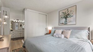 A bedroom with a bed, bedside table, nightstand, and a painting on the wall. - Waikiki Hideaway · Canal Views•Pool•Parking•W/D (Honolulu)