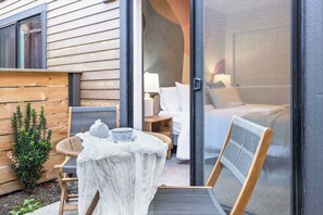 Een houten gevelwand, een schuifdeur naar een slaapkamer met een bed, een kleine tafel met een kom en een theepot, en een stoel.
