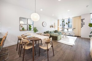 A modern living room with a dining area, a green sofa, and a large window with curtains. - Modern 3BR City View Home w/ Near Green Lake & UW (Seattle)
