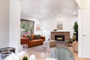A modern living room with a sofa, coffee table, fireplace, and a view of the outdoors.