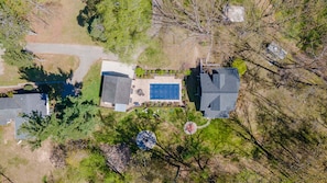 An aerial view of a residential property with a swimming pool, a fenced yard, and surrounding trees.