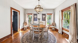 Een eetkamer met een ronde tafel, stoelen, een kroonluchter en een vloerkleed.