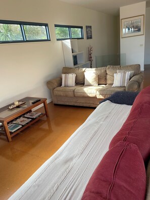 A living room with a beige sofa, a glass coffee table, and a red couch. There are two windows with blinds, a framed picture on the wall, and a bookshelf. - Sea Breeze
Charming House to stay for family getaways (Melbourne)