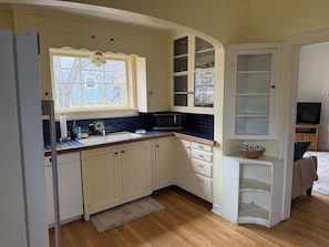 A kitchen with white cabinets, a microwave, a sink, and a window with a view of trees.