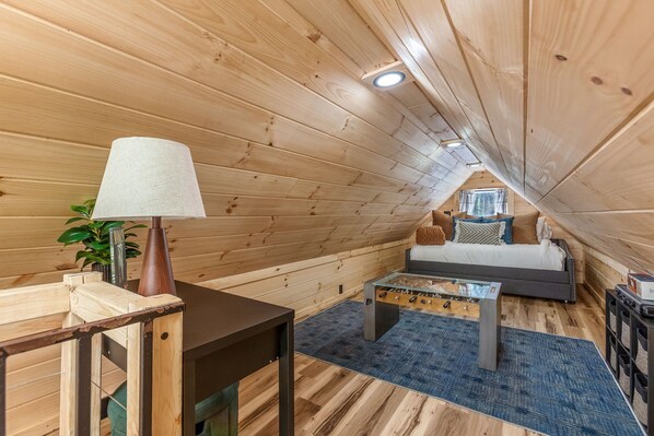 A cozy attic room with wooden walls, a sofa, a coffee table, and a lamp. - Hocking Hills~Sauna+ColdPlunge+Hot tub+Fishing Pond (Creola)