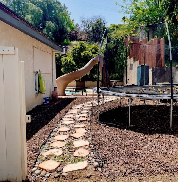 A backyard with a slide, trampoline, and stone pathway.