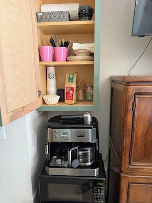 A kitchen with a coffee maker, microwave, and a cabinet with dishes and utensils.