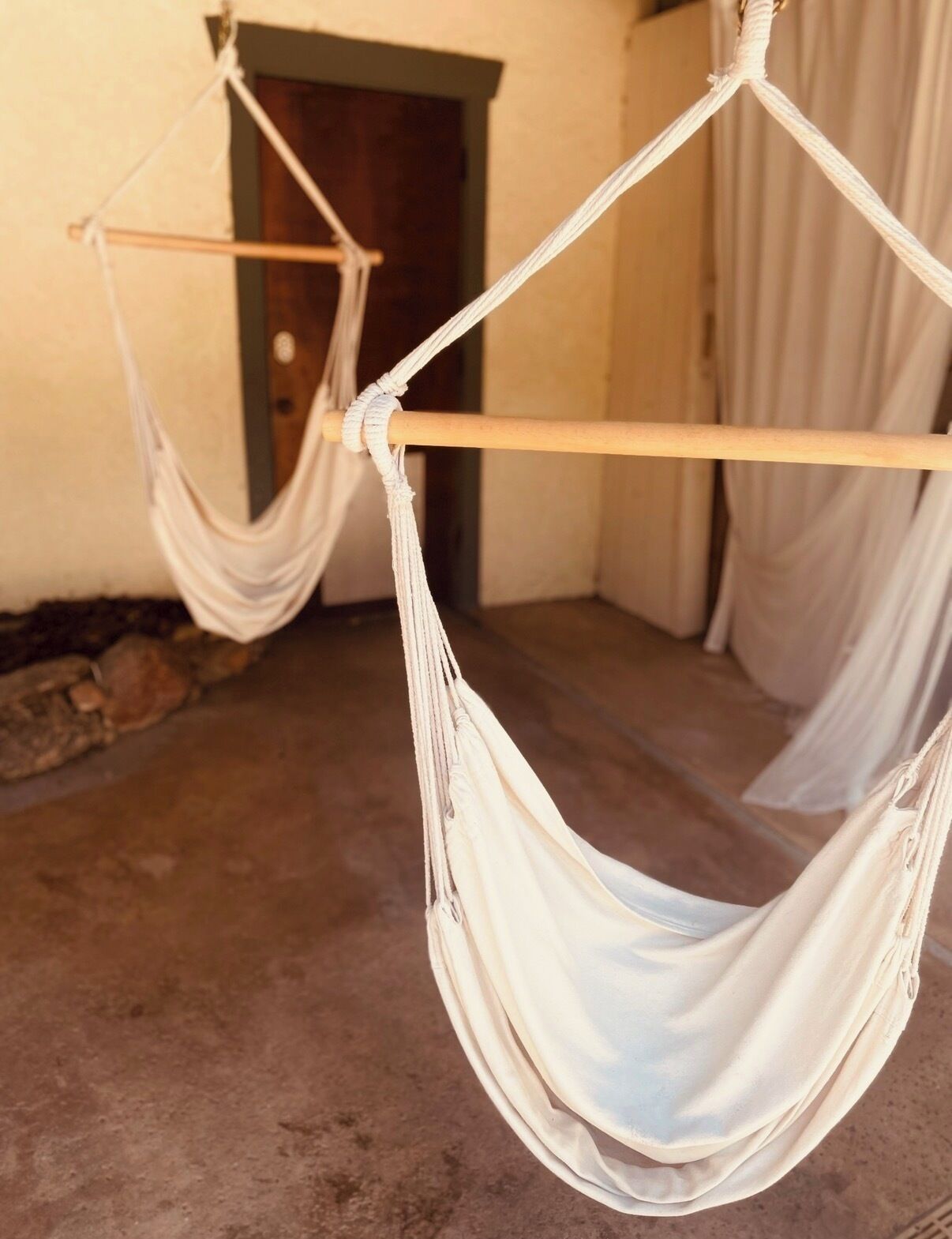 Un hamac suspendu à des cordes attachées à une poutre en bois, avec un mur de pierre et une porte en arrière-plan.