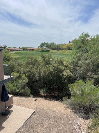 A residential area with a view of a golf course, a patio with a table and chairs, and a building with a balcony.