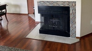 A living room with a fireplace, hardwood flooring, a dining area with a table and chairs, and a wall-mounted decorative piece.