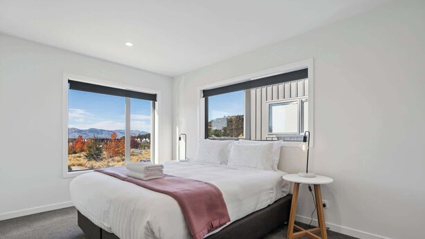 Een moderne hotelkamer met een groot bed, een nachtkastje en uitzicht op herfstkleuren en bergen.