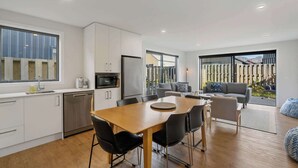 Een moderne keuken met witte kastjes, een roestvrijstalen koelkast en een eethoek met een houten tafel en zwarte stoelen.