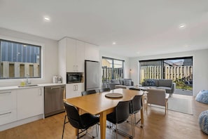 A modern kitchen with white cabinets, a stainless steel refrigerator, and a dining area with a wooden table and black chairs.