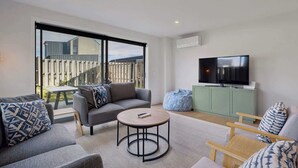 Een moderne woonkamer met een bank, fauteuil, salontafel en een televisie op een kast.
