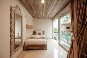 A bedroom with a wooden ceiling, a large mirror, a bed with white bedding, and a view of a pool through a large window. - Sapta Villa Ubud (Ubud)