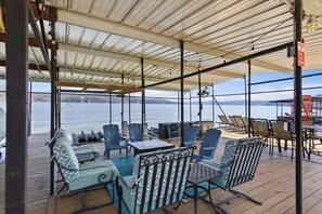 A covered outdoor seating area with chairs and tables, overlooking a body of water. - Zero-Step Dock Life with Big Views, Lake Toys, Firepit, Boat Slip at 43MM (Roach)