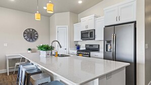 A modern kitchen with a central island, stainless steel appliances, and a clock on the wall. - Estancia Resort Unit #404 (Saint George)