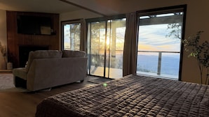 Een slaapkamer met een bed, een bank, een open haard en een grote schuifglazen deur die leidt naar een balkon met uitzicht op het water.