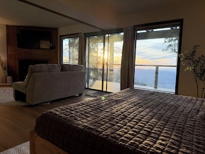 A bedroom with a bed, a sofa, a fireplace, and a large sliding glass door leading to a balcony with a view of the water. - Shaver Lake Cabin, Views, 5 Acres, Sleeps 14, A/C, Starlink Wifi (Shaver Lake)