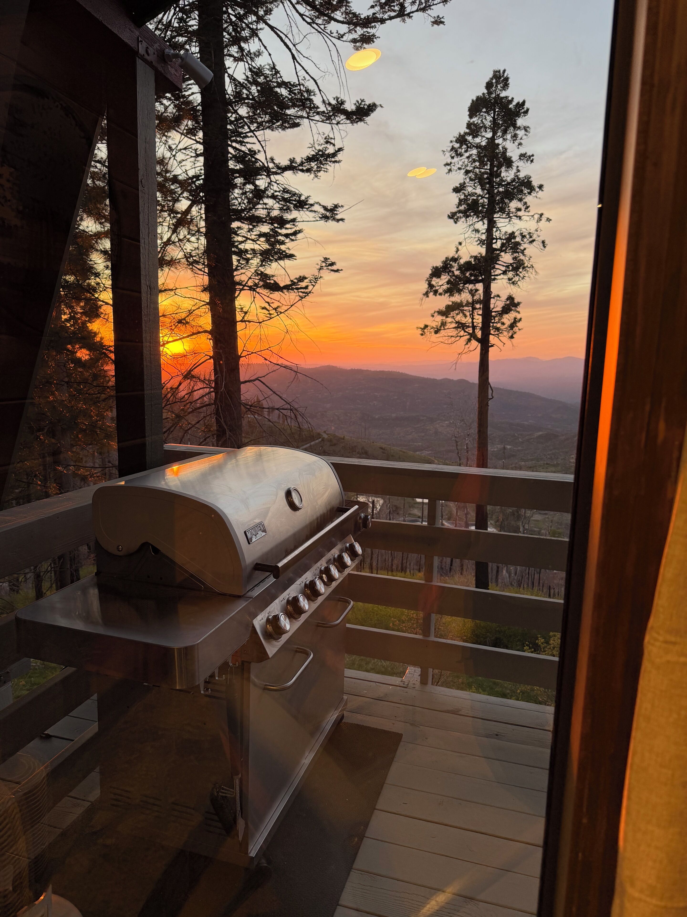 Churrasqueira em deck externo com vista para um pôr do sol e montanhas.