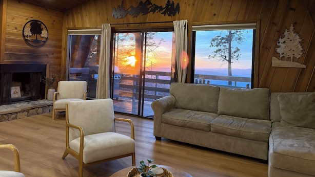 Een gezellig interieur van een blokhut met een open haard, houten wanden, een bank en uitzicht op de zonsondergang.