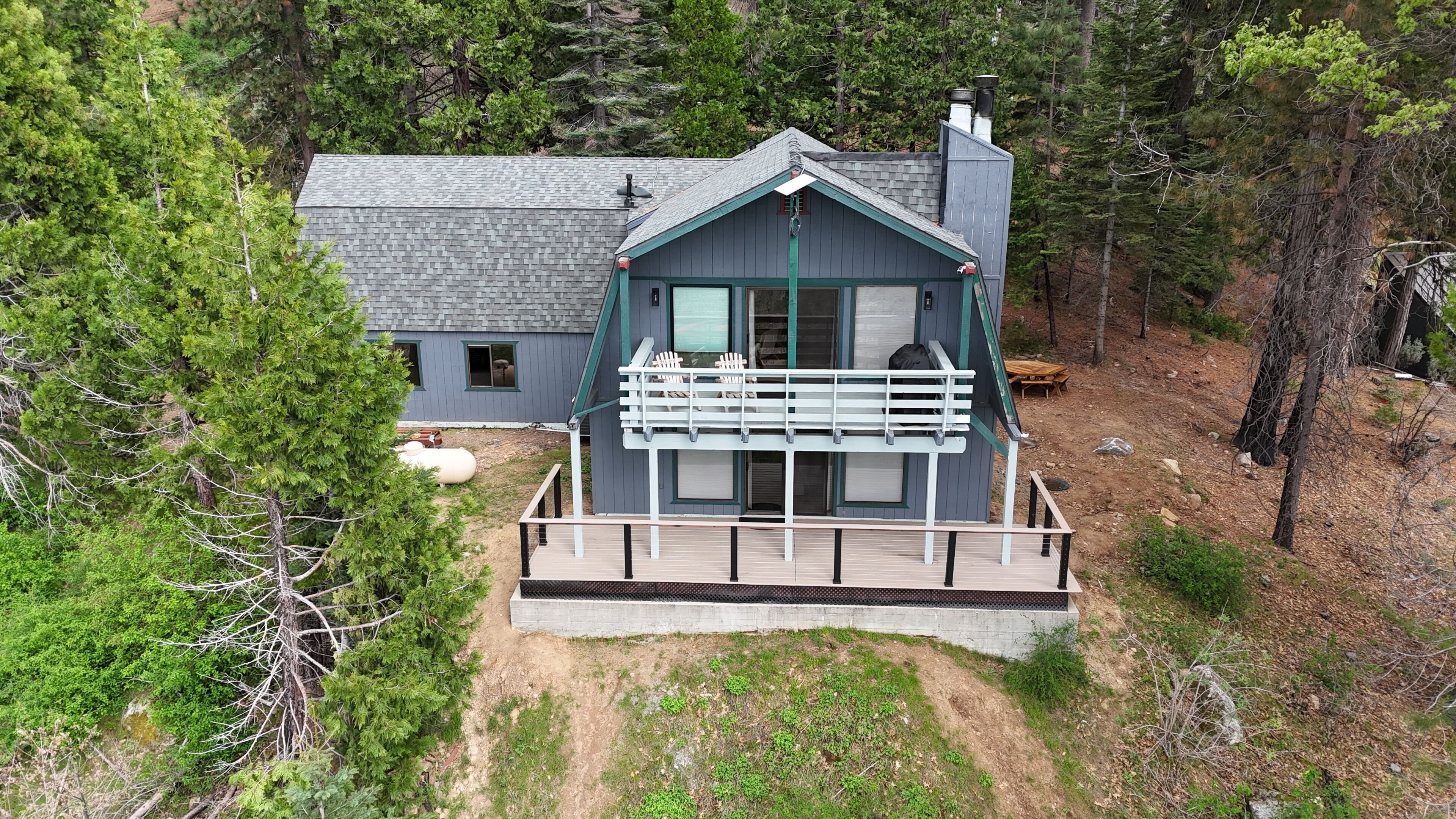 A two-story cabin with a balcony, surrounded by dense forest.