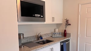 A kitchen with white cabinets, a stainless steel microwave, a sink, and a red vase. - Your Indio retreat awaits you (Indio)