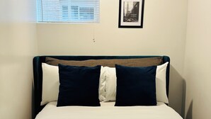 A bed with a white and dark blue headboard, two pillows, a rolled white towel, and a framed picture on the wall.