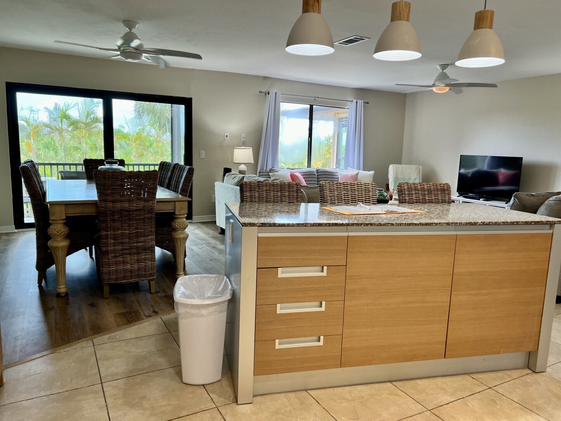 Een moderne keuken met een centraal eiland, een eetgedeelte met rieten stoelen en een televisie in de woonruimte.