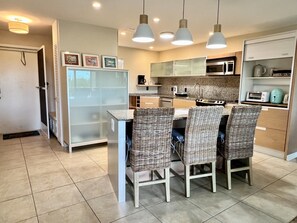 Eine moderne Küche mit Essbereich, ausgestattet mit einem Kühlschrank, einer Mikrowelle, einem Toaster, Korbstühlen und Pendelleuchten.