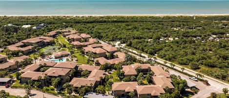 A residential area with multiple houses, a swimming pool, and a beach in the background.